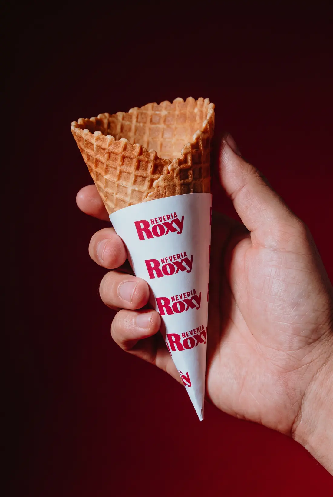 Una mano sostiene un cono de Nevería Roxy con el papel impreso de la marca