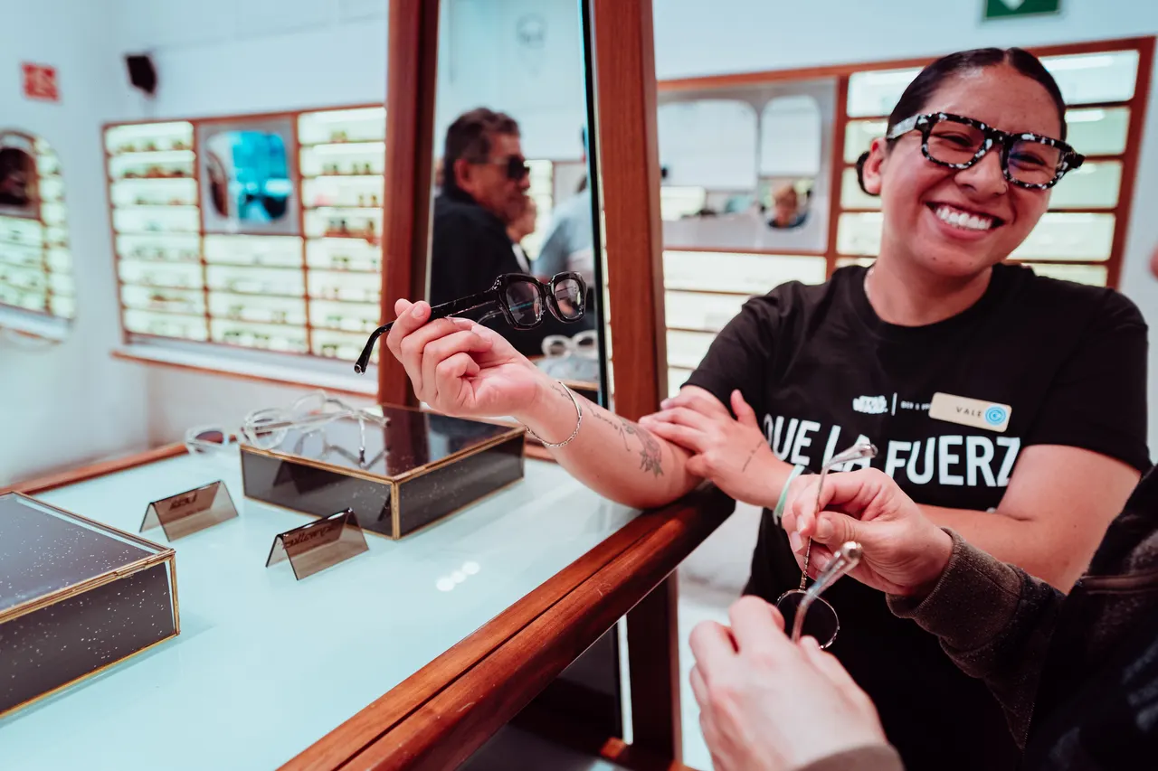 La vendedora entrega unos lentes por encima del mostrador, sonriendo