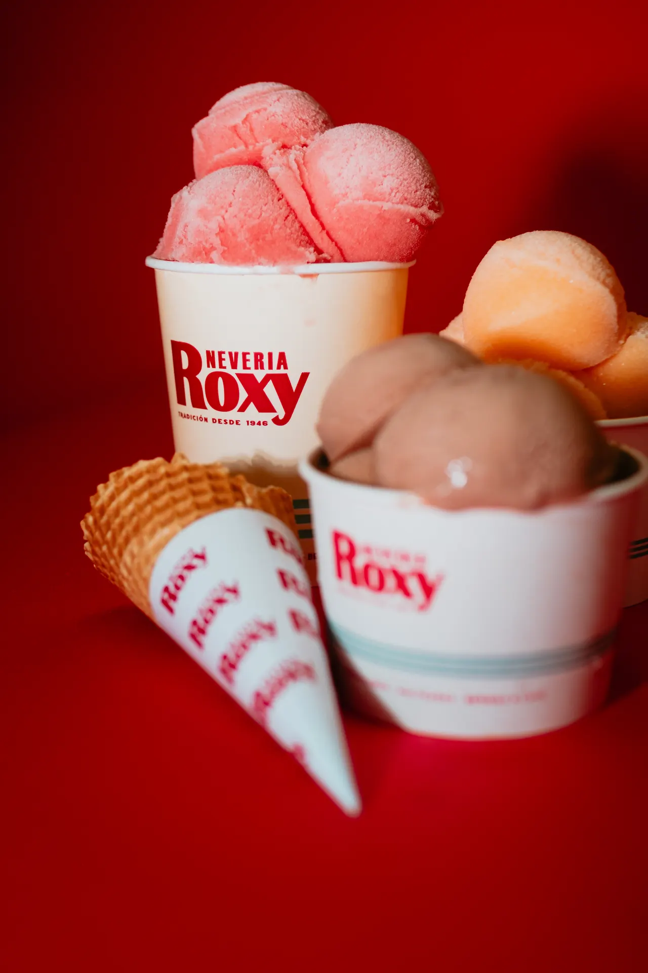 Conos y botes de Roxy con bolas de fresa, mango y chocolate, sobre el rojo de la marca