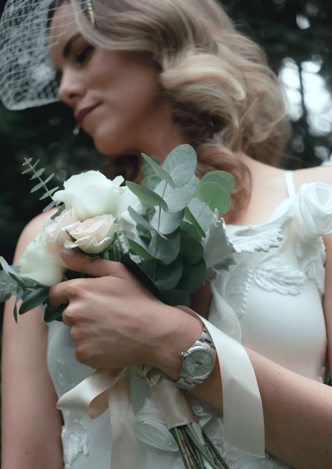 La novia, con velo de jaula, sostiene contra el hombro un ramo de rosas blancas