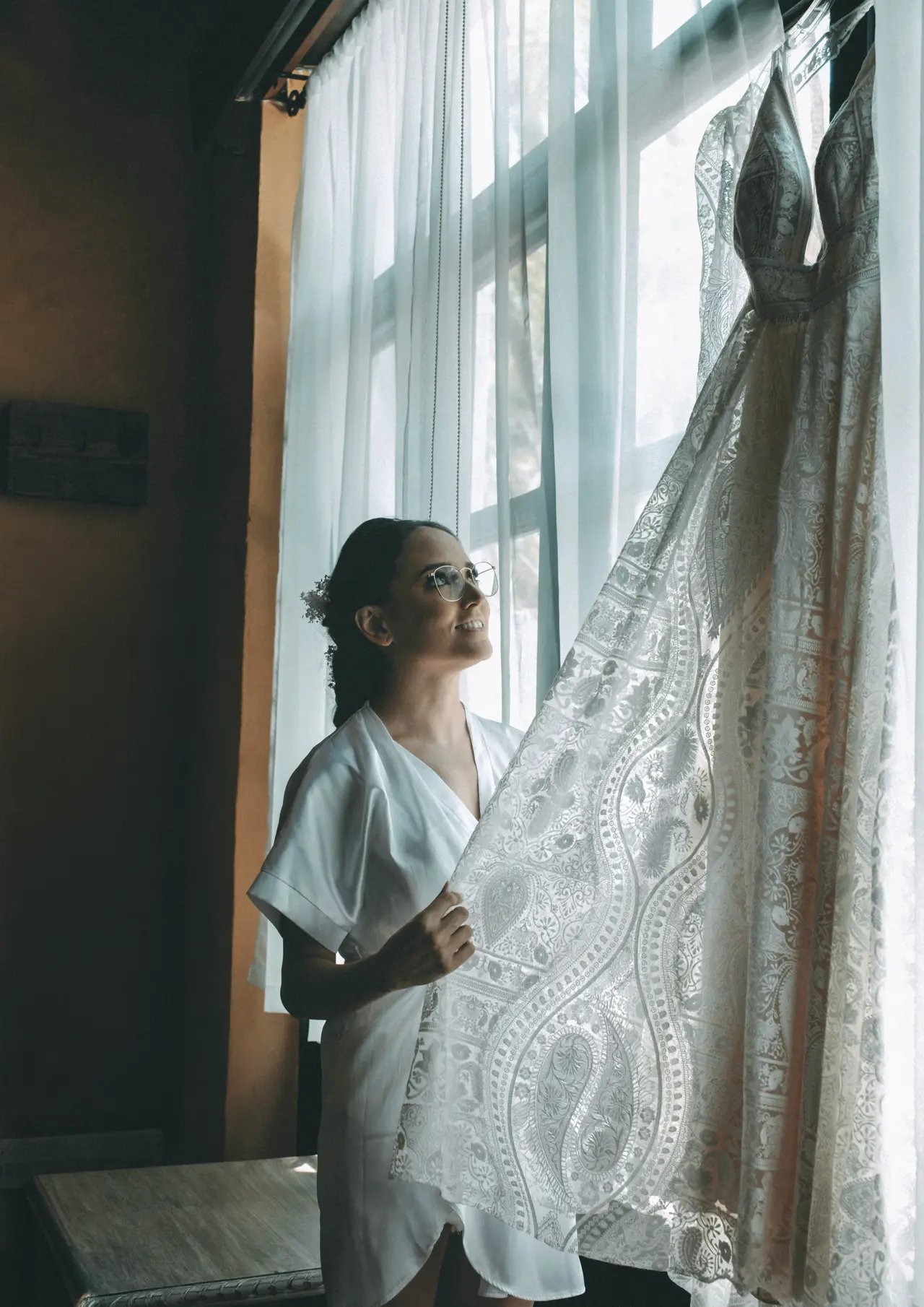 La novia junto al ventanal con el encaje del vestido en primer plano