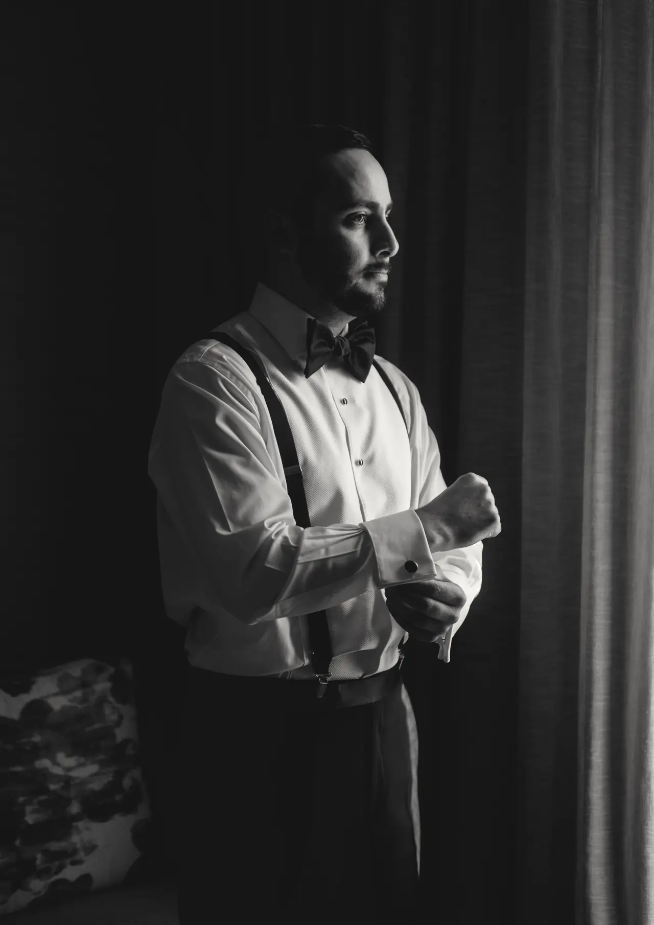 El novio abrochándose el puño de la camisa en una habitación oscura, en blanco y negro